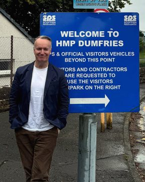 Author Andrew O'Hagan standing in front of sign for HMP Dumfries