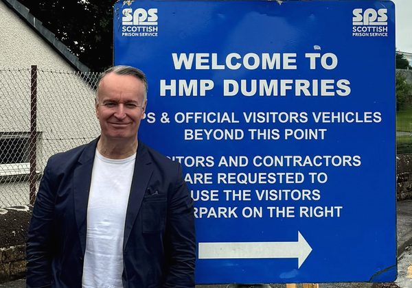 Author Andrew O'Hagan standing in front of sign for HMP Dumfries