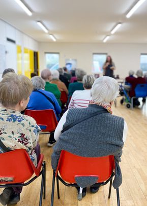 Portrait photo from back of room showing seated audience watching an author speak