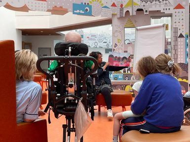 Photo from behind small audience watching author holding childrens book.
