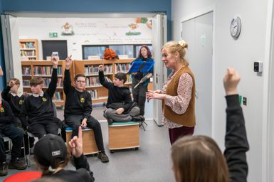School pupils with hands in the air for a question in library