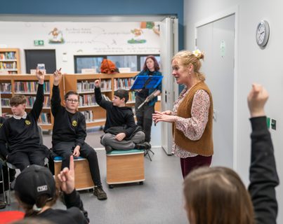School pupils with hands in the air for a question in library