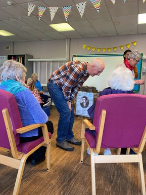 Writer Ken Cockburn bending over talking to people where we can only see the back of heads.