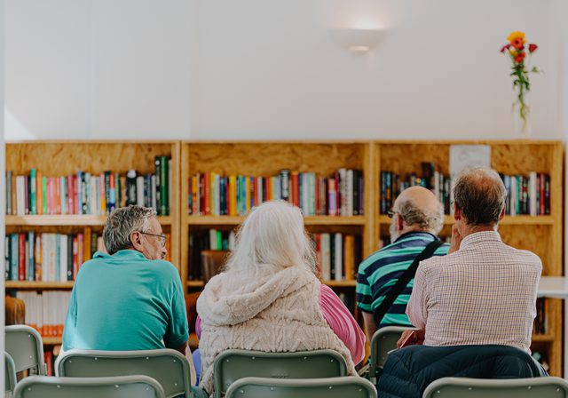 Photo from behind of four seated people facing a bookcase