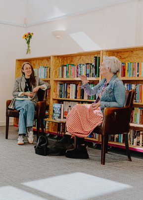 Photo of author Denise Mina on stage speaking to chairperson with a bookcase behind them at Streetreads Library