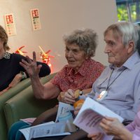 Collection of older people sitting. One has a booklet.