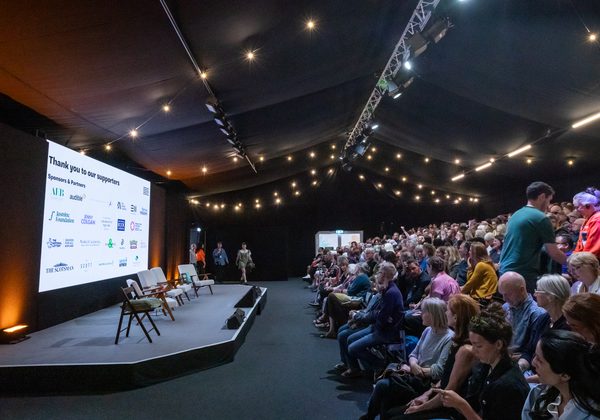 Book Festival audience on right of photo facing stage on left side with slide of Sponsors in background