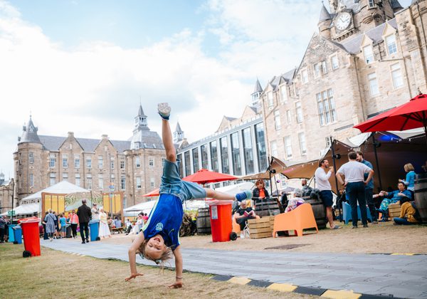 Child doing cartwheel in Book Festival courtyard with EFI building in background