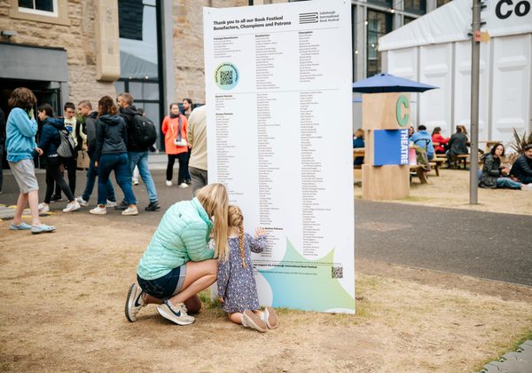 Adult and child kneeling next to sign thanking donors to the Book Festival