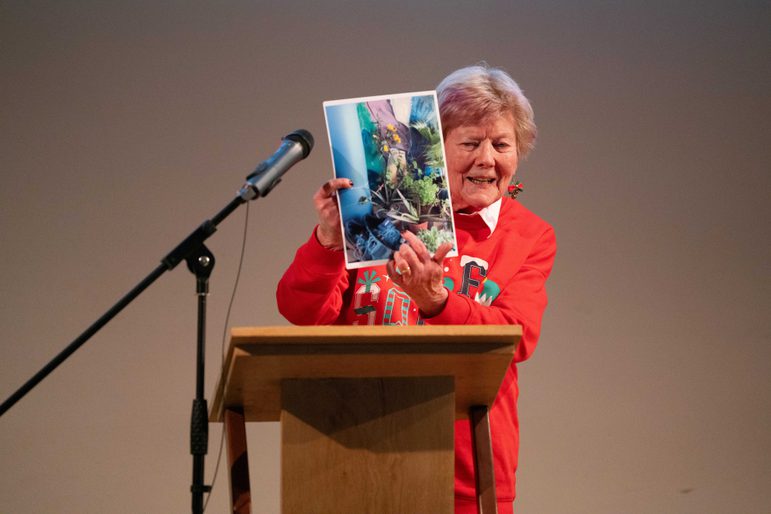 Woman speaking on stage, holding up a picture