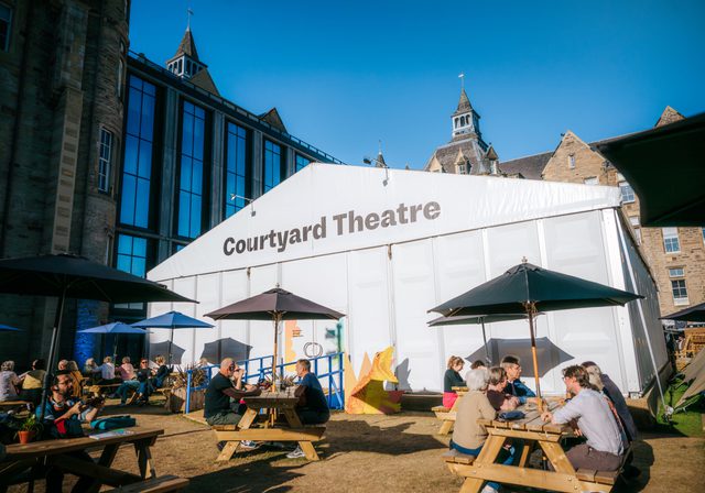 People at picnic benches outside the Book Festival Courtyard Theatre venue