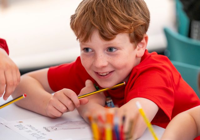 Smiling child with pencils in a pot in the foreground