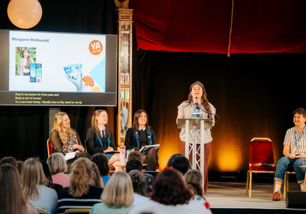 People on stage during YA Book Prize event with screen in background with YA Book Prize logo